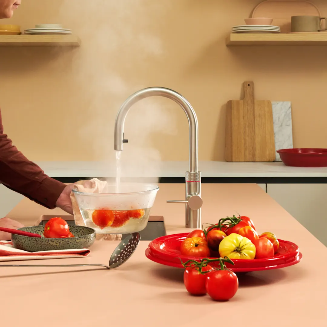 Quooker kokendwaterkraan die kokend water in een schaal met tomaten schenkt